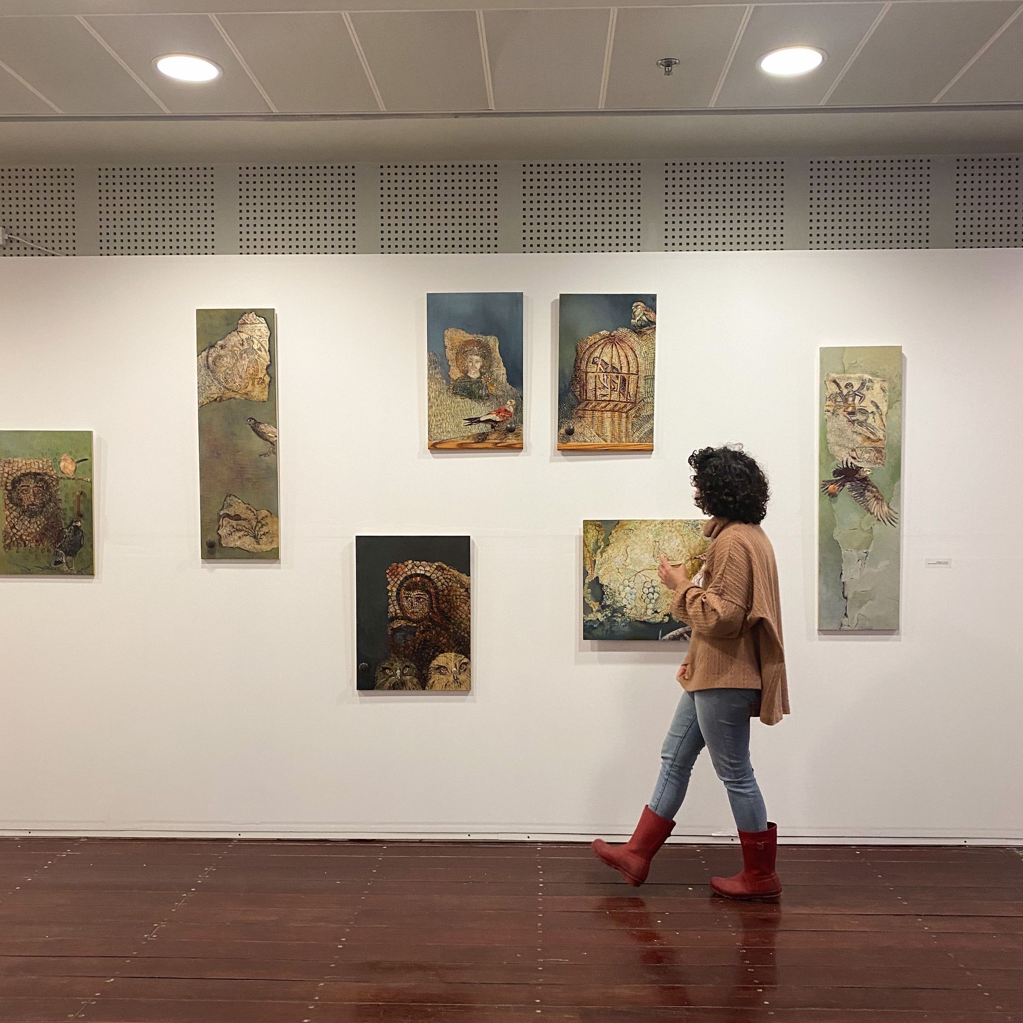 אישה מתבוננת בתמונות תלויות על הקיר במסגרת תערוכה